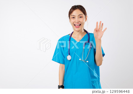 Happy friendly Asian woman nurse, clinic worker in uniform waving hi hello, a welcoming hand gesture from a smiling healthcare worker, female nurse is ready to help, isolated studio white background Happy friendly Asian woman nurse, clinic worker in uniform waving hi hello, a welcoming hand gesture from a smiling healthcare worker, female nurse is ready to help, isolated studio white background 129596448