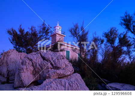 Lighthouse at dusk surrounded by coastal rocks and vegetation 129596608