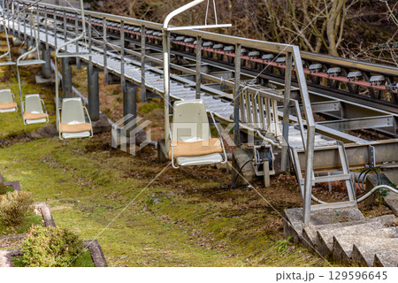 An empty ski lift chair hanging over a metal track, surrounded by trees and nature An empty ski lift chair hanging over a metal track, surrounded by trees and nature 129596645