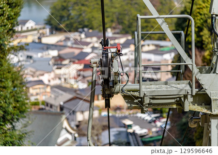 Close-up view of a cable car pulley system with a backdrop of a town and greenery 129596646