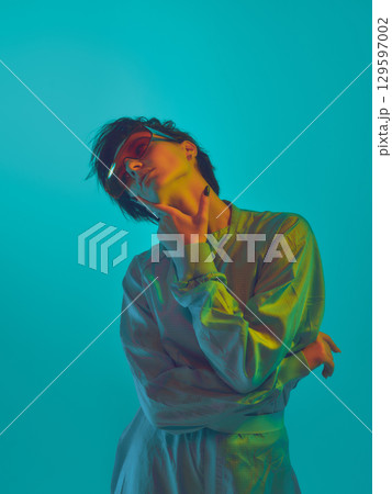 Fashion model in oversized shirt and neon visor touching face in cyan light 129597002