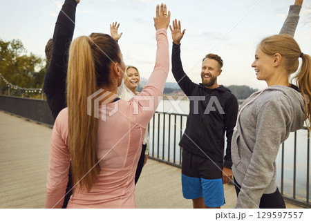 Group of happy friends high fiving each other during outdoor fitness workout in park Group of happy friends high fiving each other during outdoor fitness workout in park 129597557