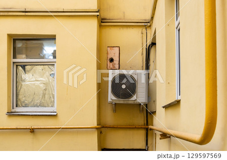 dirty air conditioner unit is mounted on a yellow wall. ventilation and cooling of the home. dirty air conditioner unit is mounted on a yellow wall. ventilation and cooling of the home. 129597569