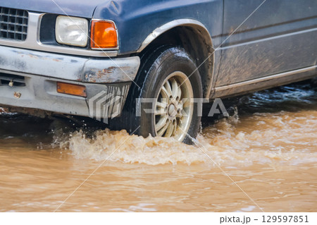 Close up of a car wheel driving through muddy red flood Close up of a car wheel driving through muddy red flood 129597851