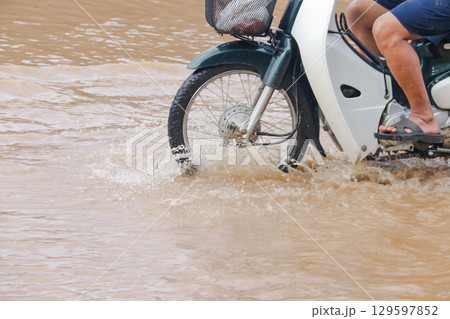 Close up of a motorcycle wheel driving through muddy red flood Close up of a motorcycle wheel driving through muddy red flood 129597852