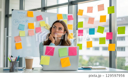 woman surrounded by colorful sticky notes, deep in thought at her desk 129597956
