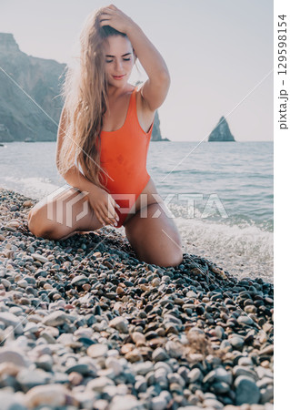 Woman in Orange Swimsuit Posing on Pebble Beach Woman in Orange Swimsuit Posing on Pebble Beach 129598154