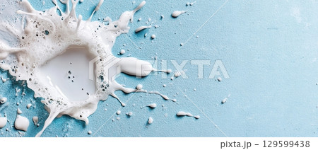White liquid splash with foam on a light blue textured background creates a dynamic and abstract design. Horizontal banner with copy space for text, poster, free space 129599438