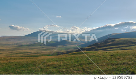 Serene landscape showcases gently rolling hills and distant mountains on a sunny day 129599782