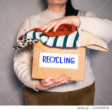 Woman holding cardboard box full of clothes labeled Recycling. Concept of sustainable fashion and responsible wardrobe management. 129599939