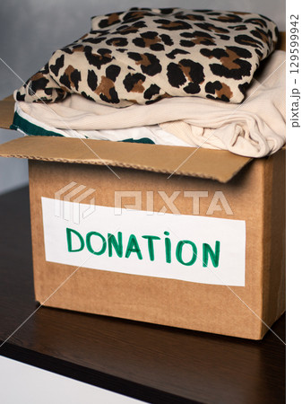 Woman folding clothes and placing them into donation box. Concept of charity and wardrobe decluttering. 129599942