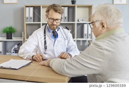 Doctor examining senior patient with fingertip pulse oximeter sitting at the desk in medical clinic 129600389