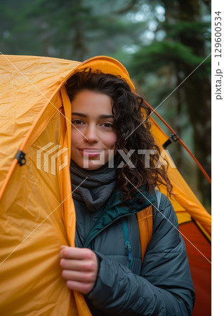 A young woman smiles from inside a cozy tent, surrounded by serene nature, embodying adventure and exploration. 129600534