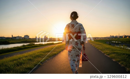 夕日を浴びながら河川敷を浴衣で歩く女性の後ろ姿美人 129600812