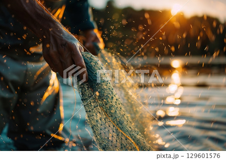 A fisherman skillfully casts a net at sunset, capturing the beauty of nature and dedication to the craft. 129601576