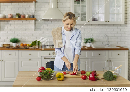 Busy woman chopping fresh vegetables for making salad, posing at kitchen Busy woman chopping fresh vegetables for making salad, posing at kitchen 129601650