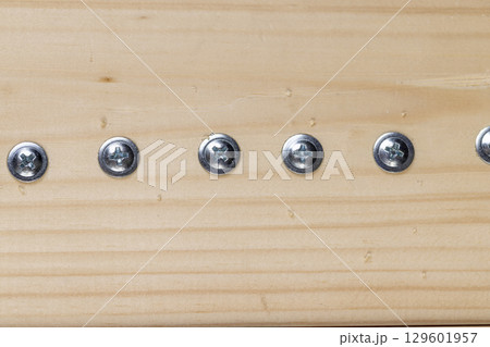 a screw screwed into a wooden board, a row of iron screws screwed into a pine board, closeup a screw screwed into a wooden board, a row of iron screws screwed into a pine board, closeup 129601957