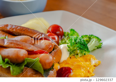 ホットドッグとスクランブルエッグ、野菜が並ぶ洋風朝食プレート 129602337