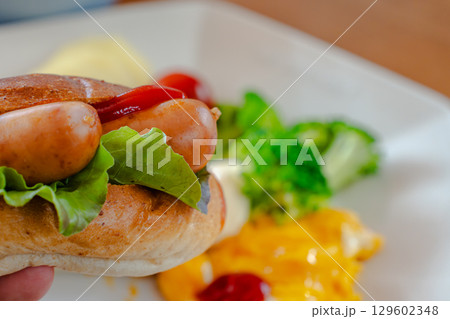 ホットドッグとスクランブルエッグ、野菜が並ぶ洋風朝食プレート 129602348
