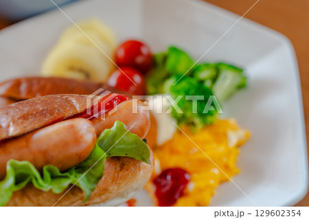 ホットドッグとスクランブルエッグ、野菜が並ぶ洋風朝食プレート ホットドッグとスクランブルエッグ、野菜が並ぶ洋風朝食プレート 129602354