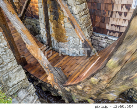 Rotating water mill. Old wooden water mill. Mill wheel rotating under stream of water at village 129603504