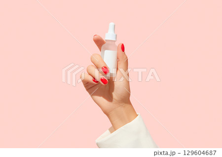 Womans hand holding white cosmetic dropper on pink background. Cosmetics sale concept 129604687