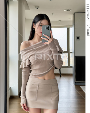 鏡越しに自撮りをするベージュコーデの女性 129605111
