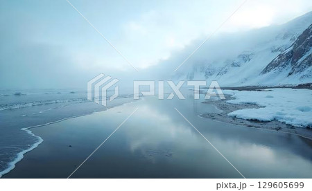 A picturesque beach featuring reflective waters and snow-dusted mountains in the distance, blending warmth and coolness 129605699