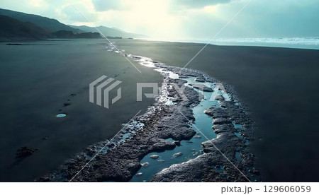 A long, narrow stream of water flows gently along the sandy beach in a serene landscape setting 129606059