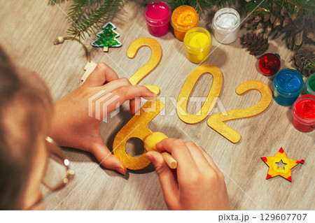 Children's hands paint yellow color wooden toy number six with spruce branches, pinecones and and other figures of new year on table 129607707