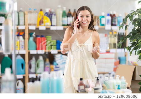 Woman consults mobile phone to choose household items in supermarket 129608686