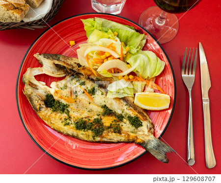 Grilled seabass with fresh salad and lemon on red plate 129608707