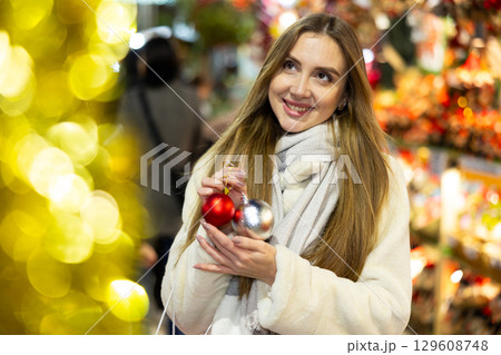 Girl with ball for Christmas tree in her hands stands in middle of New Year market Girl with ball for Christmas tree in her hands stands in middle of New Year market 129608748