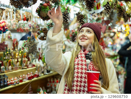 Young woman in souvenir shop examines Christmas handmade toys Young woman in souvenir shop examines Christmas handmade toys 129608750