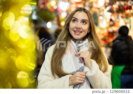 Cute woman walking through evening Christmas market on city street Cute woman walking through evening Christmas market on city street 129608818