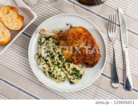 Czech cuisine. Fried duck leg with wheat porridge (perlovka) with spinach served on plate 129608851