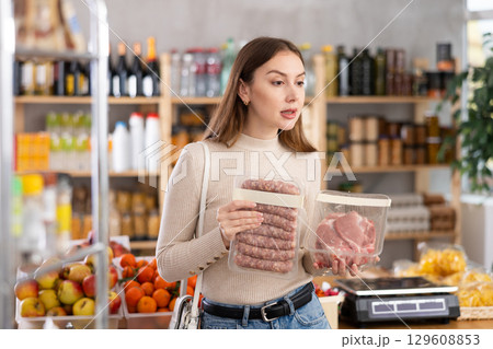 Girl looking at raw bbg sausage and raw pork chop in store 129608853