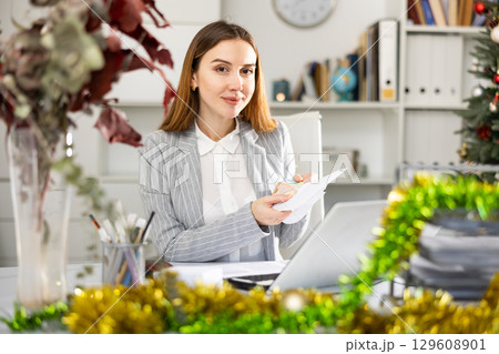 Woman office worker with wage packet in Christmas decorated office Woman office worker with wage packet in Christmas decorated office 129608901