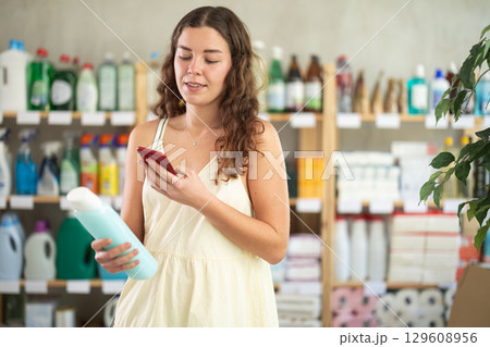 Young woman in summer clothes scanning QR-code on shampoo in store 129608956