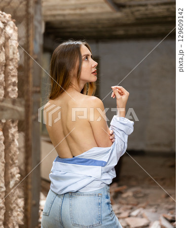 Rear view of woman standing in shirt with bare back inside destroyed building 129609142