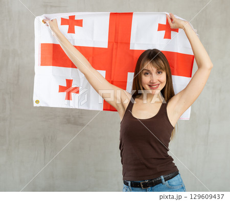Happy young woman holding flag of Georgia against unicoloured background 129609437