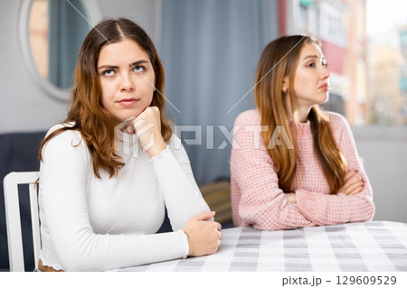 Upset woman sitting at home table with disgruntled woman behind Upset woman sitting at home table with disgruntled woman behind 129609529