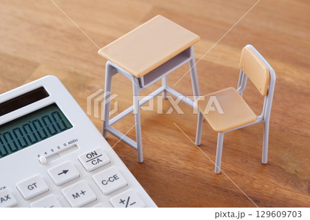 学校の机と椅子、電卓がイメージする、高騰を続けて家計を圧迫する教育費のイメージ 129609703