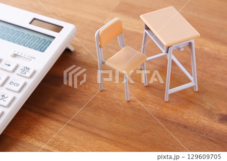 学校の机と椅子、電卓がイメージする、高騰を続けて家計を圧迫する教育費のイメージ 129609705
