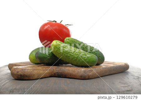 Fresh cucumbers and tomato lying on wooden cutting board 129610279