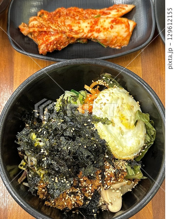 Sizzling hot dolsot bibimbap served in a stone pot with crispy rice, colorful vegetables, marinated meat, a fried egg, and gochujang. A Korean dish full of flavor and texture. 129612155
