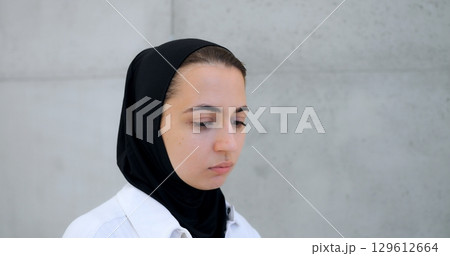 Professional businesswoman wearing hijab, standing confidently near concrete wall, expressing range of emotions while looking directly toward camera Professional businesswoman wearing hijab, standing confidently near concrete wall, expressing range of emotions while looking directly toward camera 129612664