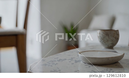 Stylish ceramic cup and saucer slowly spin on a beautiful marble coffee table, showcasing elegant tableware in a contemporary living room setting 129612810