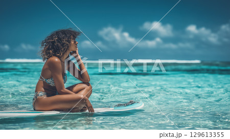 Woman sitting on surfboard in clear blue sea under sunny sky 129613355