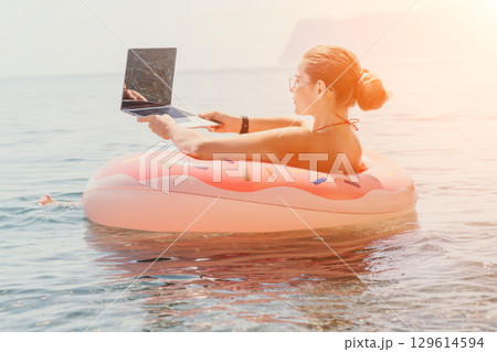 Woman, Laptop, Beach: Working on laptop while floating on an inflatable ring in the ocean. Woman, Laptop, Beach: Working on laptop while floating on an inflatable ring in the ocean. 129614594